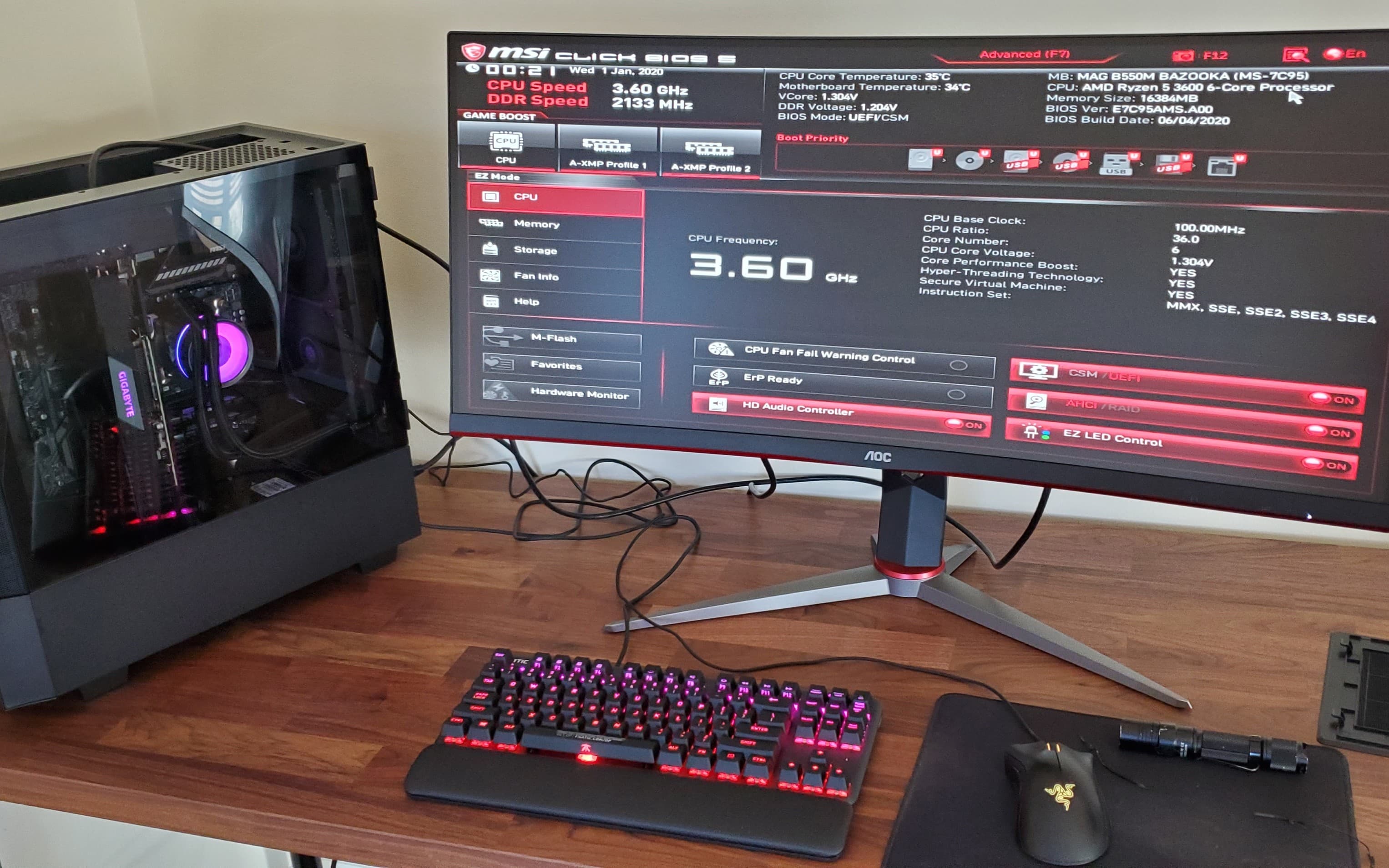 Powered-on darkFlash PC beside a monitor displaying MSI BIOS with the Ryzen 5 3600 and 16 GB of memory detected